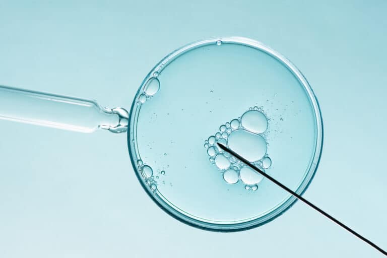A glass petri dish with blue liquid and bubbles, crossed by a long slender instrument.