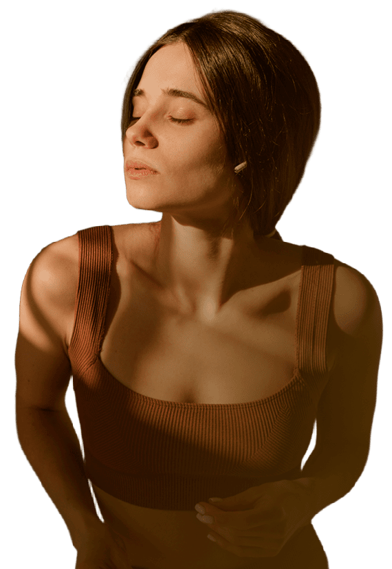 Woman with short brown hair, eyes closed, wearing a ribbed brown tank top, basking in warm sunlight.