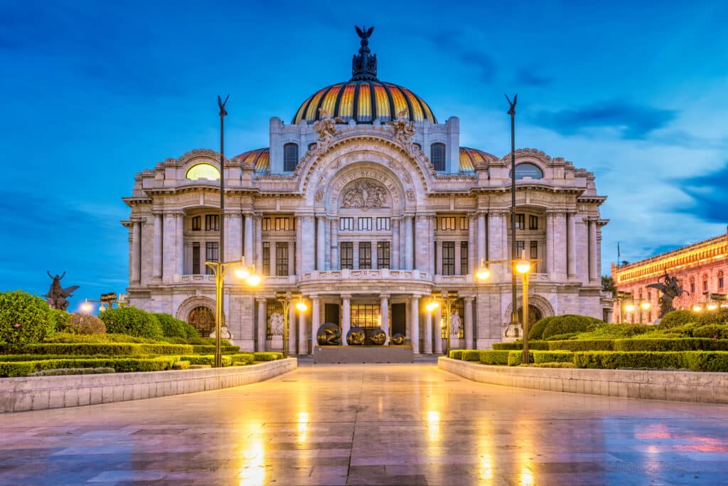 National Palace of Arts architectural facade with a large central dome, ornate arches, statues, and manicured gardens at dusk