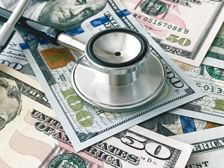 A stethoscope placed on scattered U.S. currency, including tens and fives, suggesting a link between medicine and money.