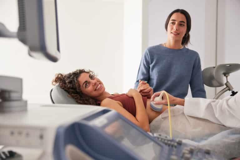 Couple holding hands during a fertility clinic ultrasound consultation while weighing IVF costs