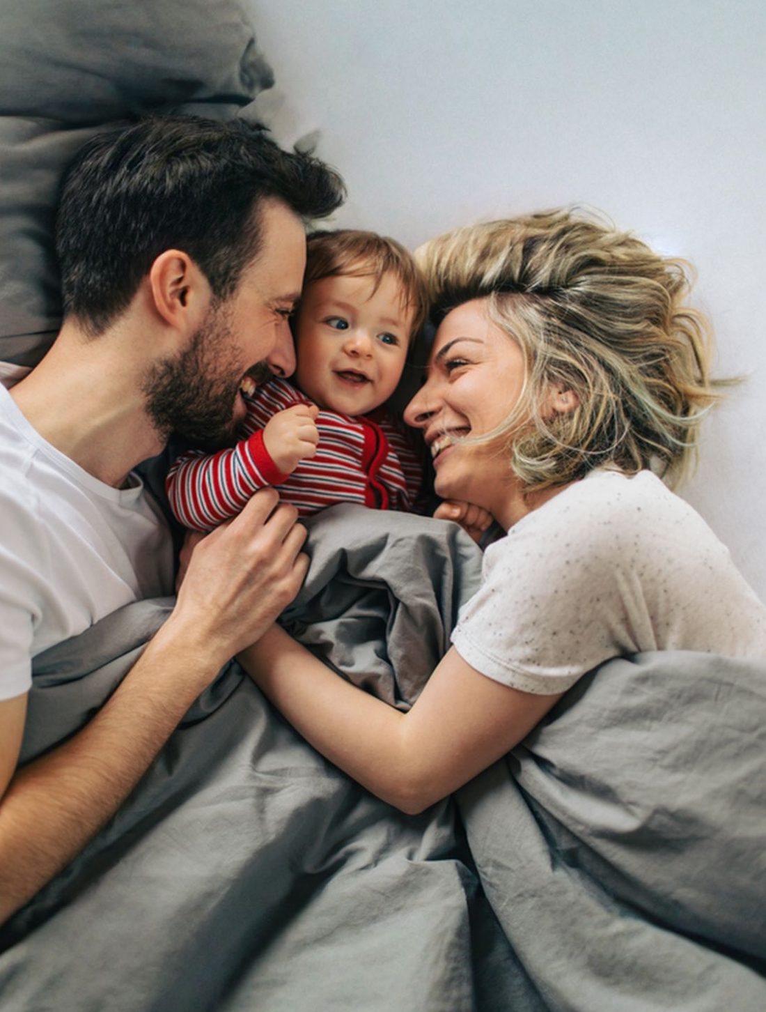 Young parents laughing with their baby in bed on a slow morning at home